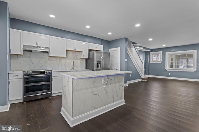 kitchen featuring dark wood-style flooring, white cabinets, under cabinet range hood, appliances with stainless steel finishes, and backsplash