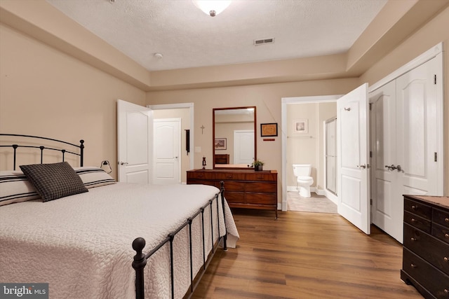 bedroom featuring visible vents, dark wood-type flooring, ensuite bathroom, a closet, and a textured ceiling