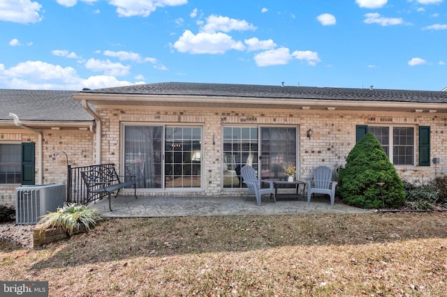 rear view of property featuring a patio, brick siding, central AC, and a shingled roof