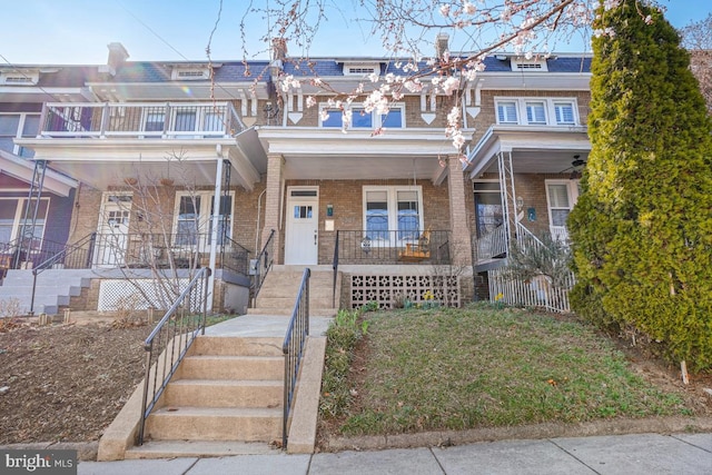 view of property featuring mansard roof, brick siding, covered porch, and stairs