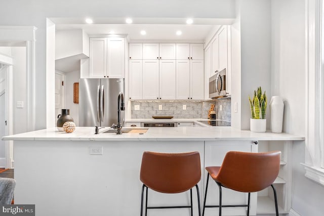 kitchen featuring a breakfast bar area, light stone counters, white cabinets, appliances with stainless steel finishes, and backsplash