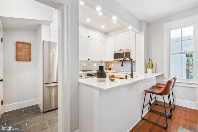 kitchen with tasteful backsplash, appliances with stainless steel finishes, white cabinets, light countertops, and baseboards