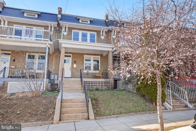 townhome / multi-family property with brick siding, stairway, covered porch, and mansard roof