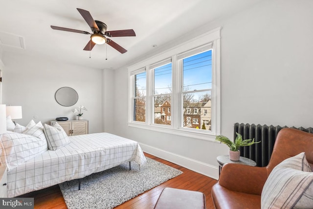 bedroom featuring a ceiling fan, radiator, wood finished floors, and baseboards