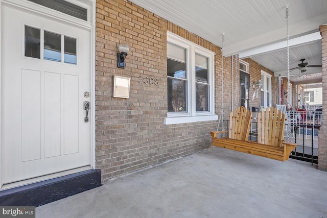 view of exterior entry with brick siding, covered porch, and a ceiling fan