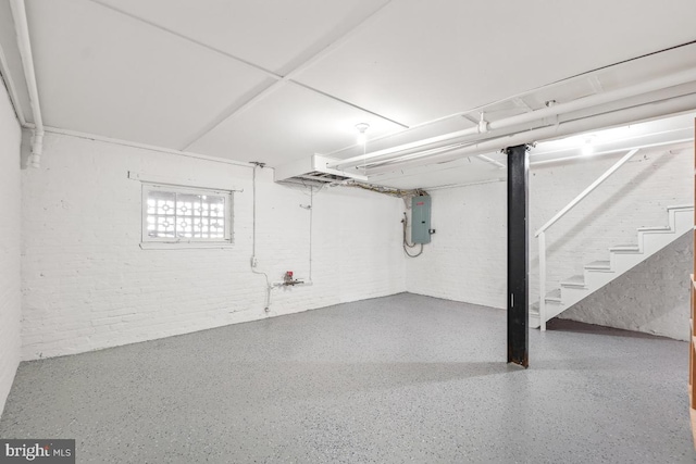 basement featuring electric panel, brick wall, and stairs