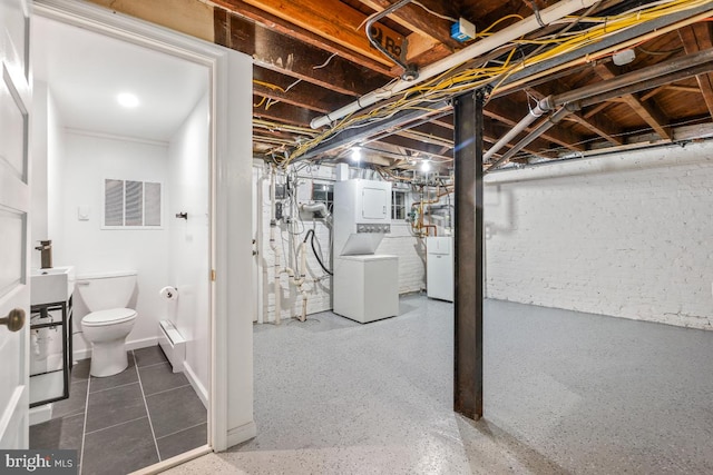 unfinished below grade area with visible vents, baseboard heating, and stacked washer and dryer