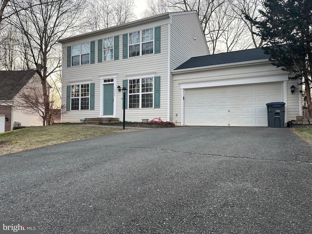 colonial home with a front yard, an attached garage, and driveway