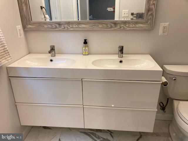 bathroom featuring double vanity, marble finish floor, toilet, and a sink