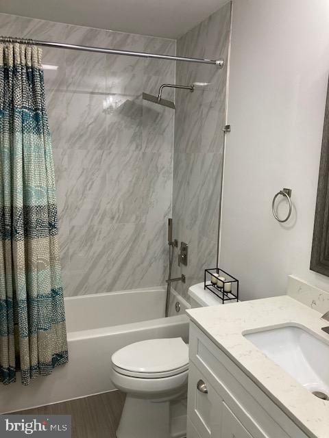 bathroom with vanity, wood finished floors, toilet, and shower / bathtub combination with curtain