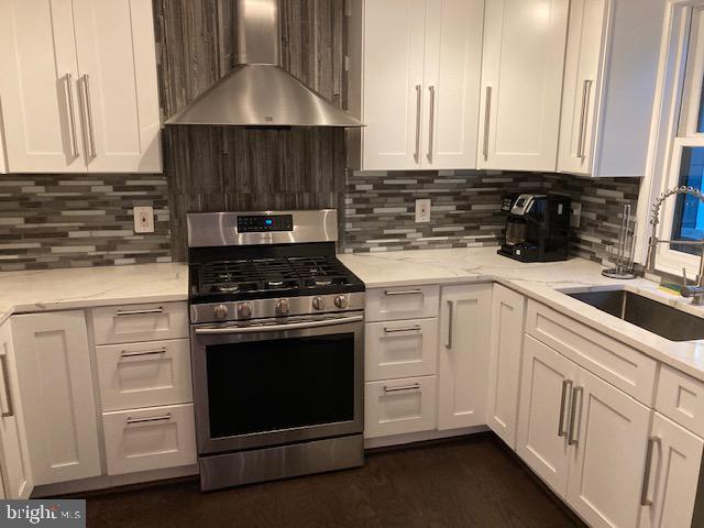 kitchen with stainless steel range with gas stovetop, white cabinets, wall chimney exhaust hood, and a sink