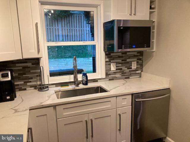 kitchen featuring a sink, decorative backsplash, appliances with stainless steel finishes, and white cabinets