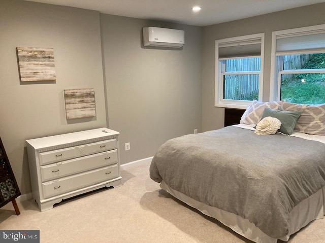 bedroom with recessed lighting, baseboards, light carpet, and an AC wall unit