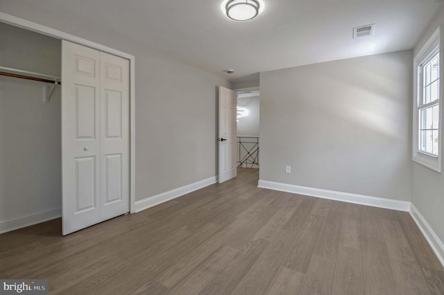 unfurnished bedroom with visible vents, wood finished floors, baseboards, and a closet