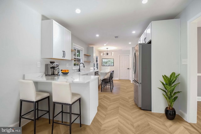 kitchen featuring a breakfast bar, recessed lighting, a peninsula, freestanding refrigerator, and a sink