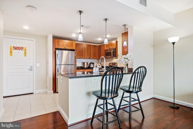 kitchen with visible vents, light wood-style flooring, stainless steel appliances, a peninsula, and brown cabinetry