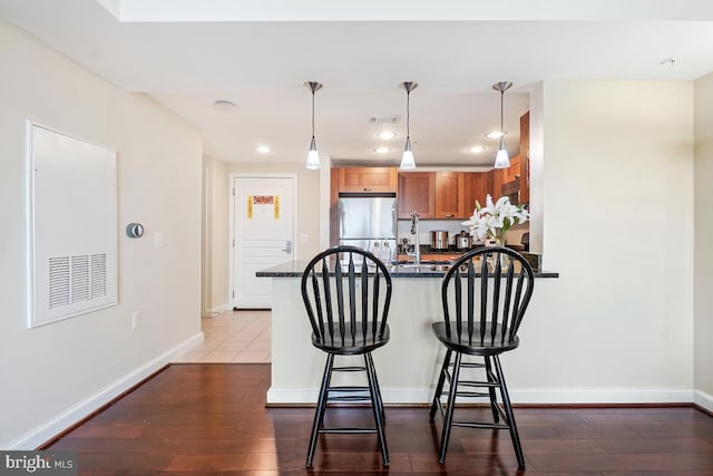 kitchen with baseboards, visible vents, dark wood finished floors, a peninsula, and freestanding refrigerator