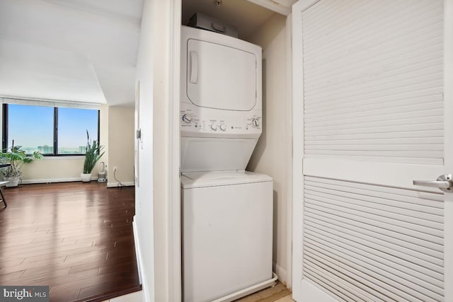 clothes washing area with baseboards, stacked washer and clothes dryer, wood finished floors, and laundry area