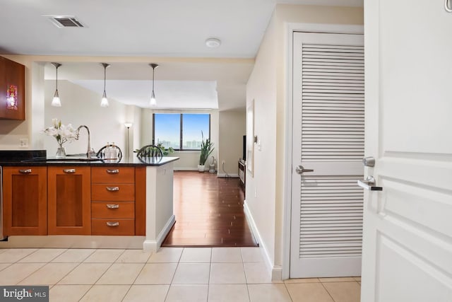kitchen with visible vents, light tile patterned floors, hanging light fixtures, brown cabinetry, and a sink