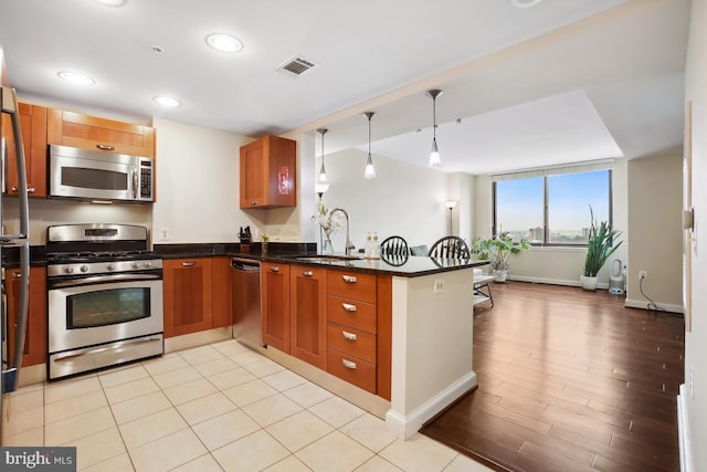 kitchen with visible vents, a peninsula, a sink, stainless steel appliances, and pendant lighting