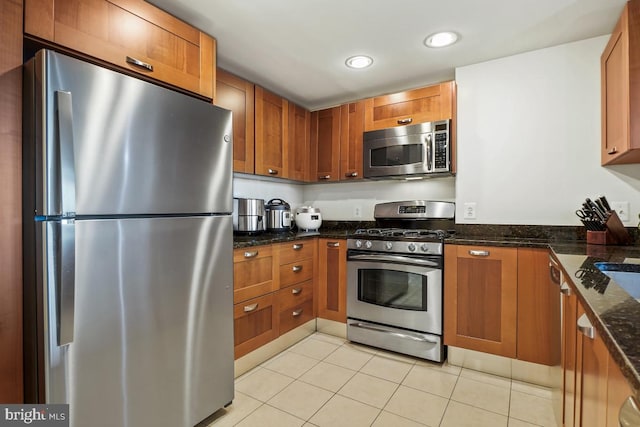 kitchen featuring dark stone countertops, stainless steel appliances, light tile patterned flooring, and brown cabinetry