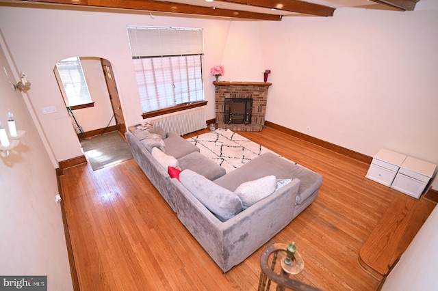 living room with baseboards, arched walkways, beam ceiling, and hardwood / wood-style floors