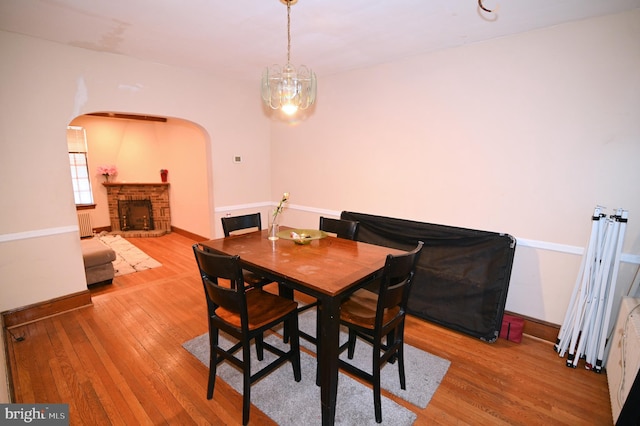 dining space featuring a brick fireplace, radiator heating unit, arched walkways, and wood-type flooring