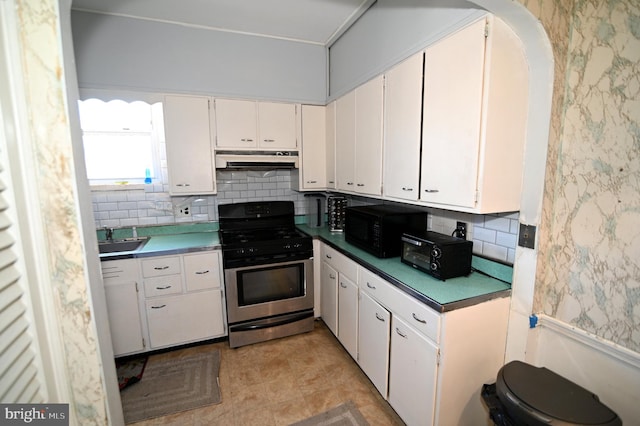 kitchen featuring under cabinet range hood, a sink, black microwave, decorative backsplash, and gas range