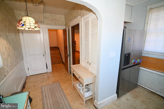 corridor featuring stairway, radiator, light floors, wallpapered walls, and arched walkways