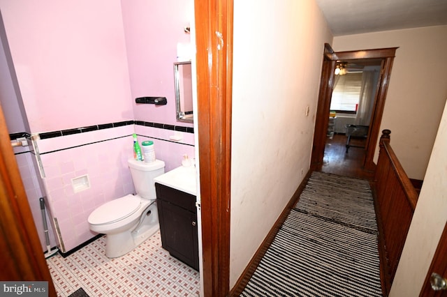 half bath featuring toilet, tile walls, wainscoting, and vanity