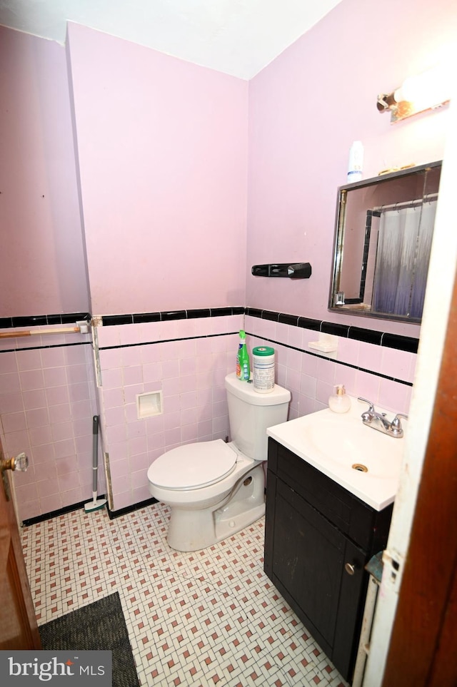 bathroom with tile walls, wainscoting, toilet, and vanity