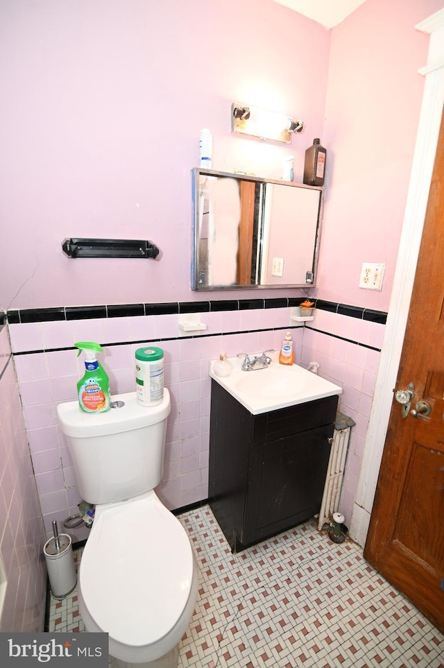 bathroom with a wainscoted wall, toilet, vanity, and tile walls