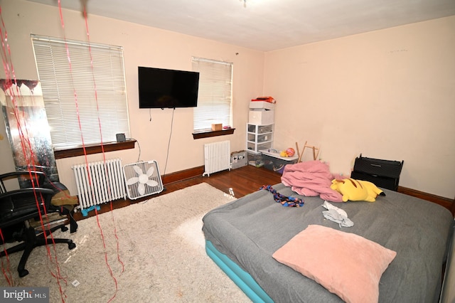 bedroom with radiator heating unit, wood finished floors, and baseboards