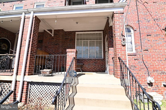 entrance to property with covered porch and brick siding