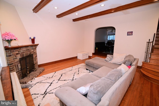 living room featuring wood finished floors, baseboards, beam ceiling, arched walkways, and a brick fireplace