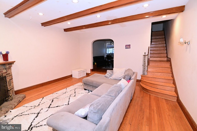 living area with beamed ceiling, wood finished floors, stairway, arched walkways, and a brick fireplace