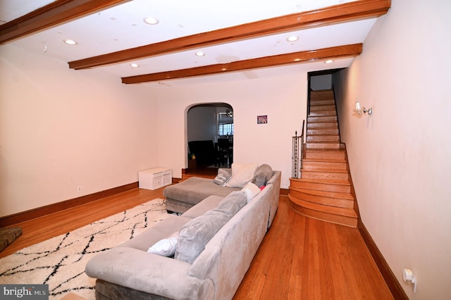 living area featuring arched walkways, beam ceiling, light wood-style flooring, and stairway