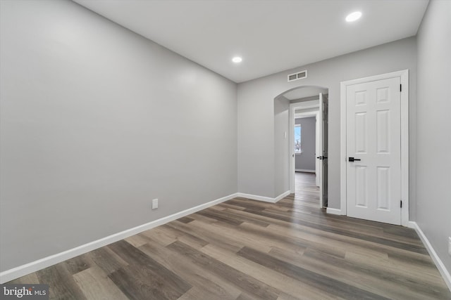 unfurnished room featuring wood finished floors, visible vents, arched walkways, and baseboards