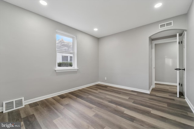 empty room featuring wood finished floors, arched walkways, visible vents, and baseboards