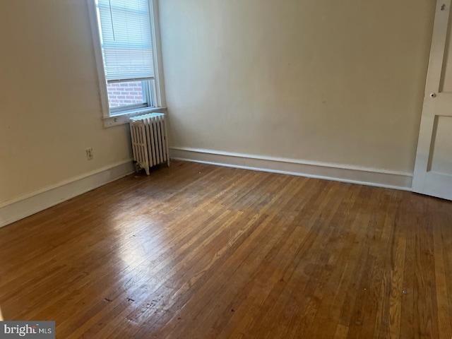 empty room featuring hardwood / wood-style floors, radiator heating unit, and baseboards