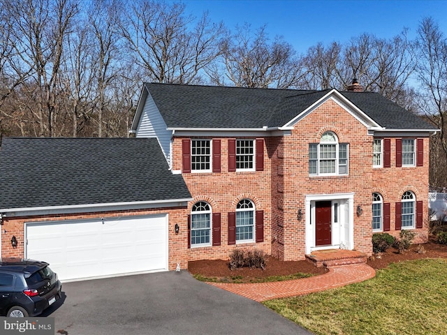 colonial inspired home featuring a garage, brick siding, driveway, and a chimney