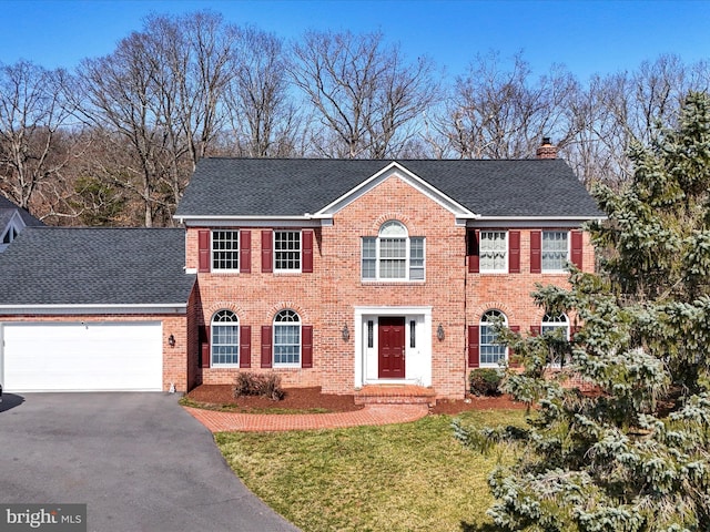 colonial house featuring a garage, brick siding, a chimney, and aphalt driveway