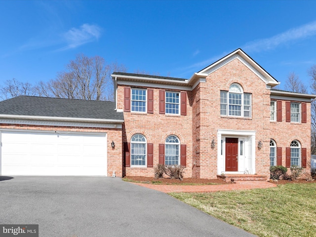 view of front of home with aphalt driveway, an attached garage, brick siding, and a front yard