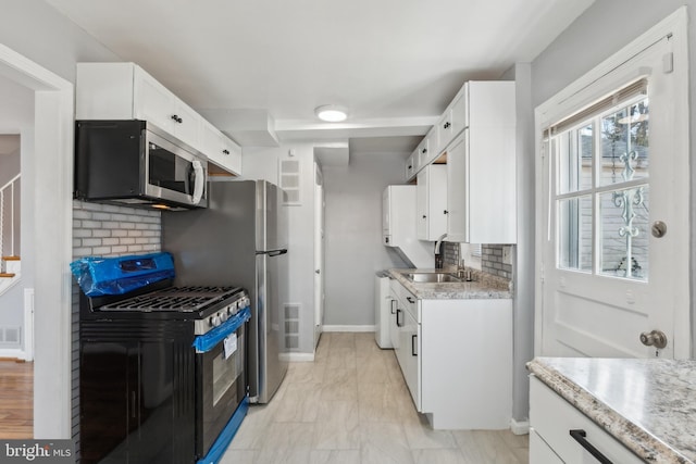 kitchen featuring a sink, stainless steel microwave, backsplash, white cabinetry, and gas range