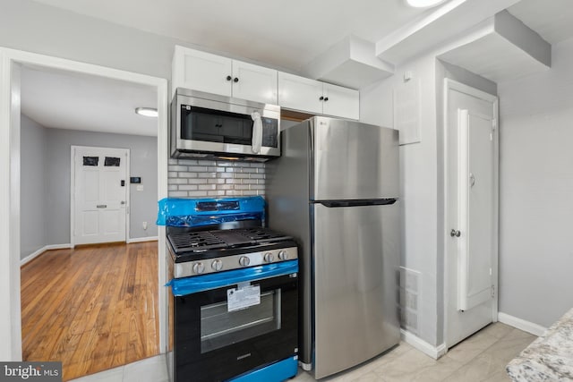 kitchen featuring baseboards, stainless steel appliances, white cabinetry, light wood-type flooring, and backsplash