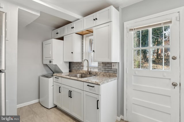 kitchen with baseboards, decorative backsplash, white cabinetry, stacked washer / drying machine, and a sink