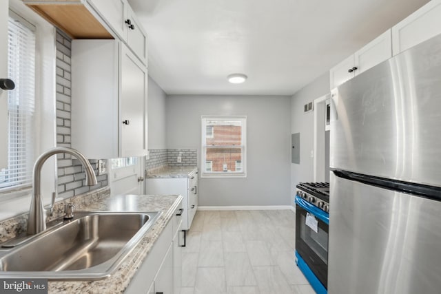 kitchen with freestanding refrigerator, a sink, white cabinets, gas range, and tasteful backsplash