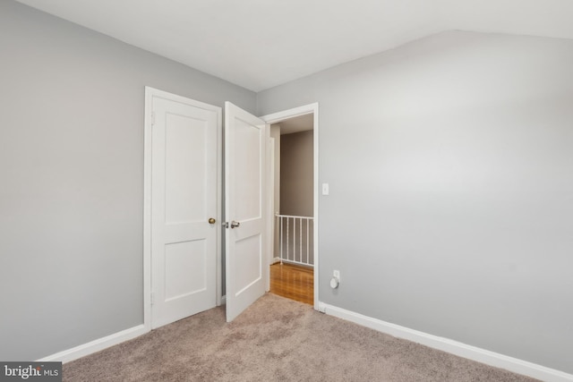 unfurnished room featuring vaulted ceiling, baseboards, and light carpet