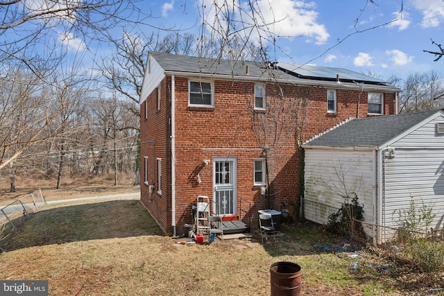 rear view of property featuring a yard, cooling unit, brick siding, and roof mounted solar panels