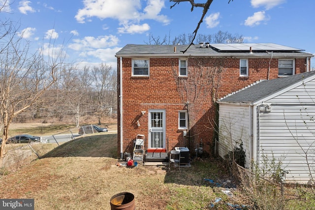 back of property with brick siding, solar panels, a yard, and fence